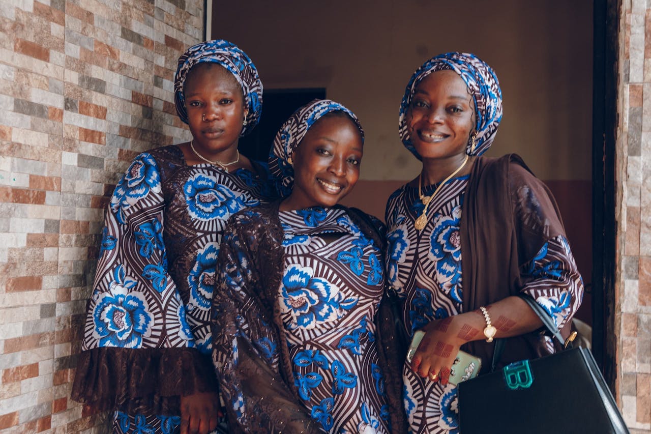 Crafting Captivating Headlines: Your awesome post title goes here Three smiling women in matching blue and brown traditional African attire posing indoors.