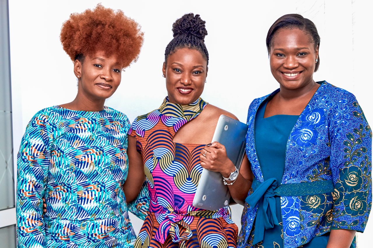 Mastering the First Impression: Your intriguing post title goes here Three diverse businesswomen smiling in vibrant attire, showing teamwork indoors.